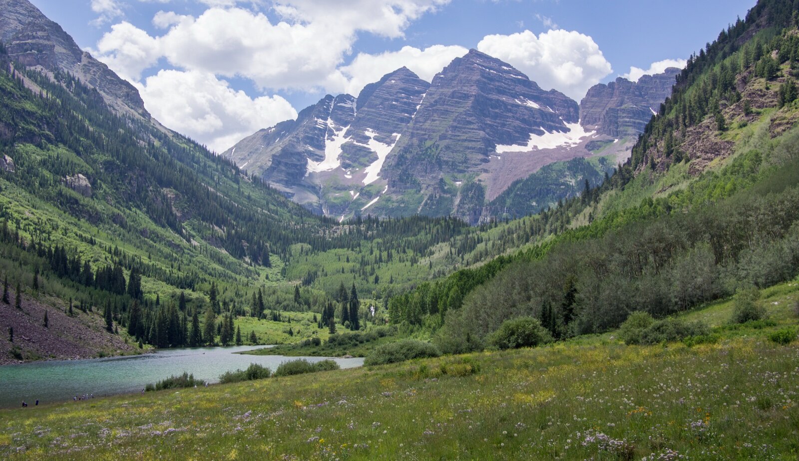 The Maroon Bells peaks above a green valley and lake near Aspen, Colorado