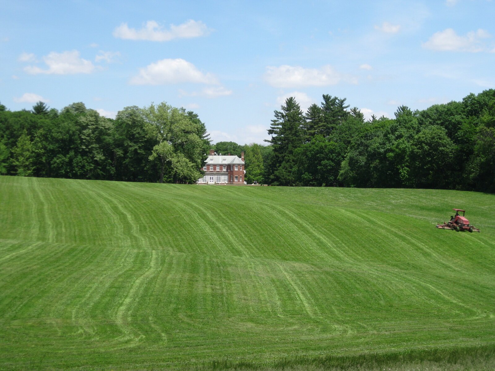 The red-brick Allerton Mansion seen across a wide, freshly mown meadow ringed by woods in Monticello, Illinois