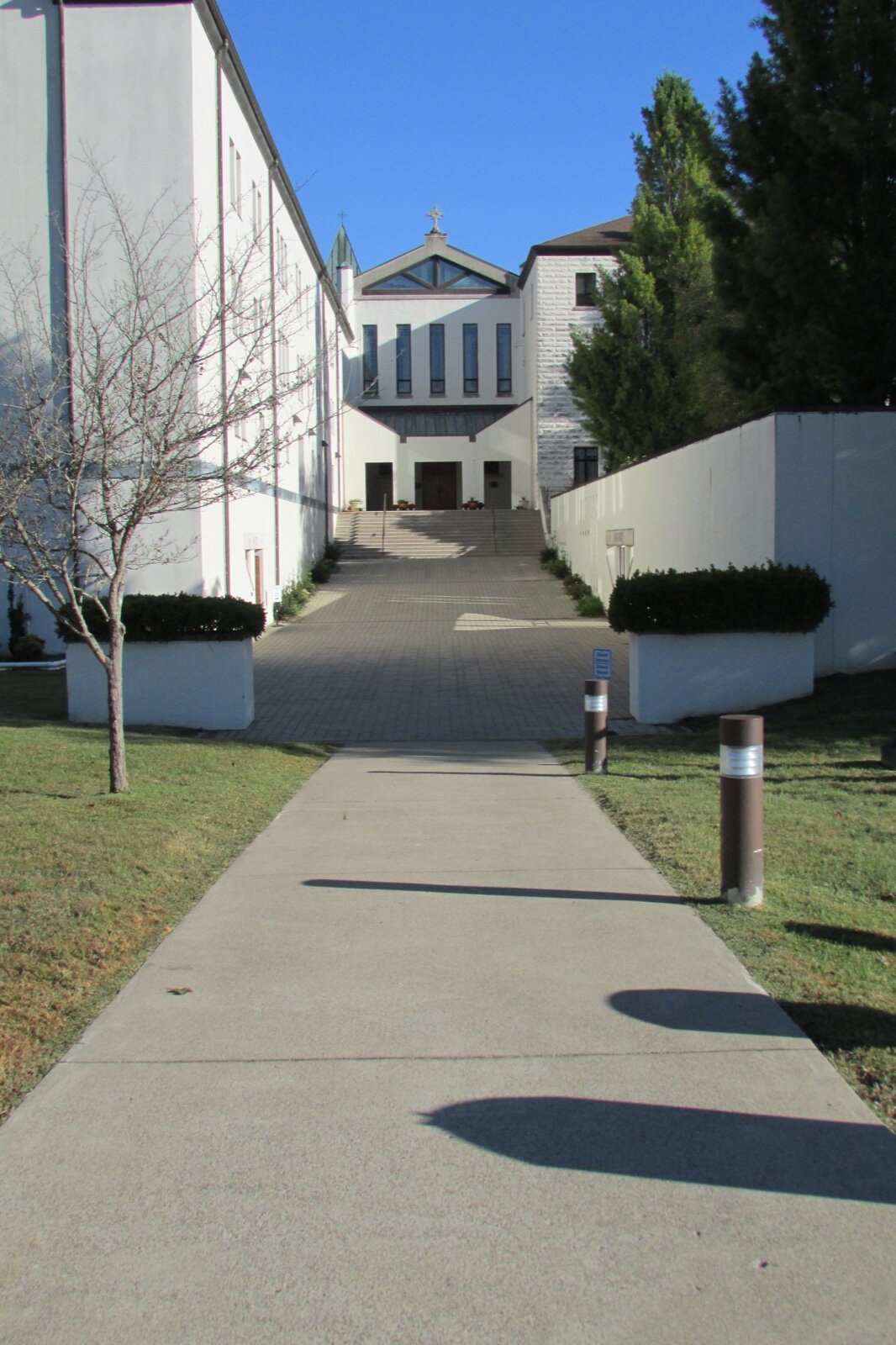 A paved walkway between white buildings leading to the abbey church at the Abbey of Gethsemani in Kentucky