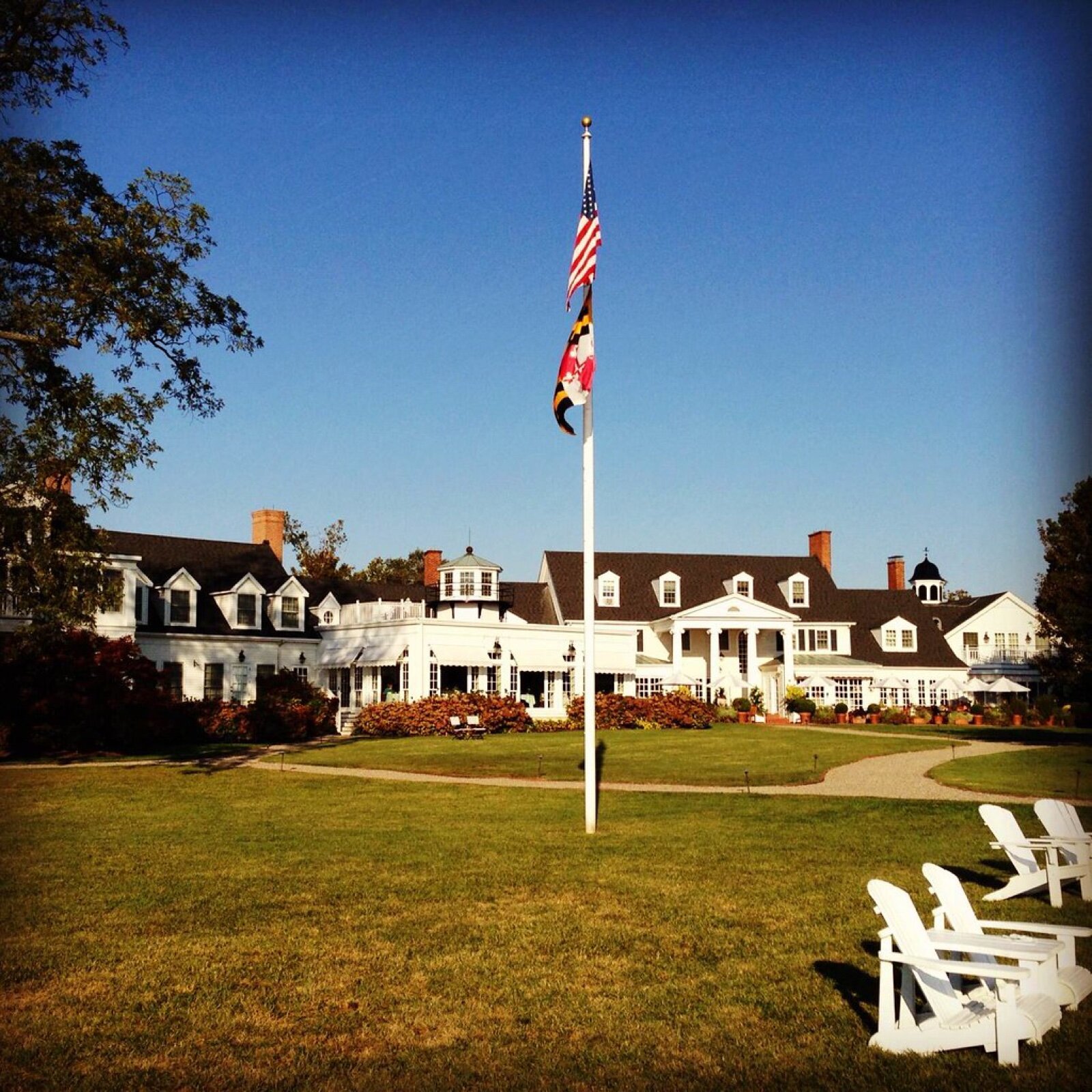 The white clapboard Inn at Perry Cabin in St. Michaels, Maryland, with a flagpole and Adirondack chairs on the lawn