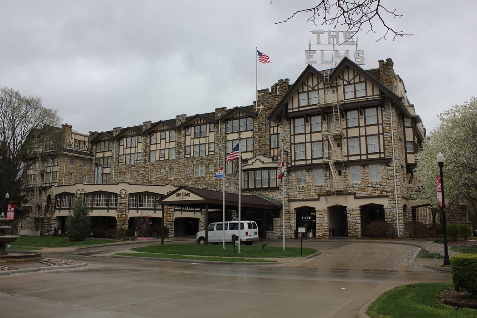 The stone and timber facade of The Elms Hotel in Excelsior Springs, Missouri, with flags at the entrance and the hotel's name on the roof