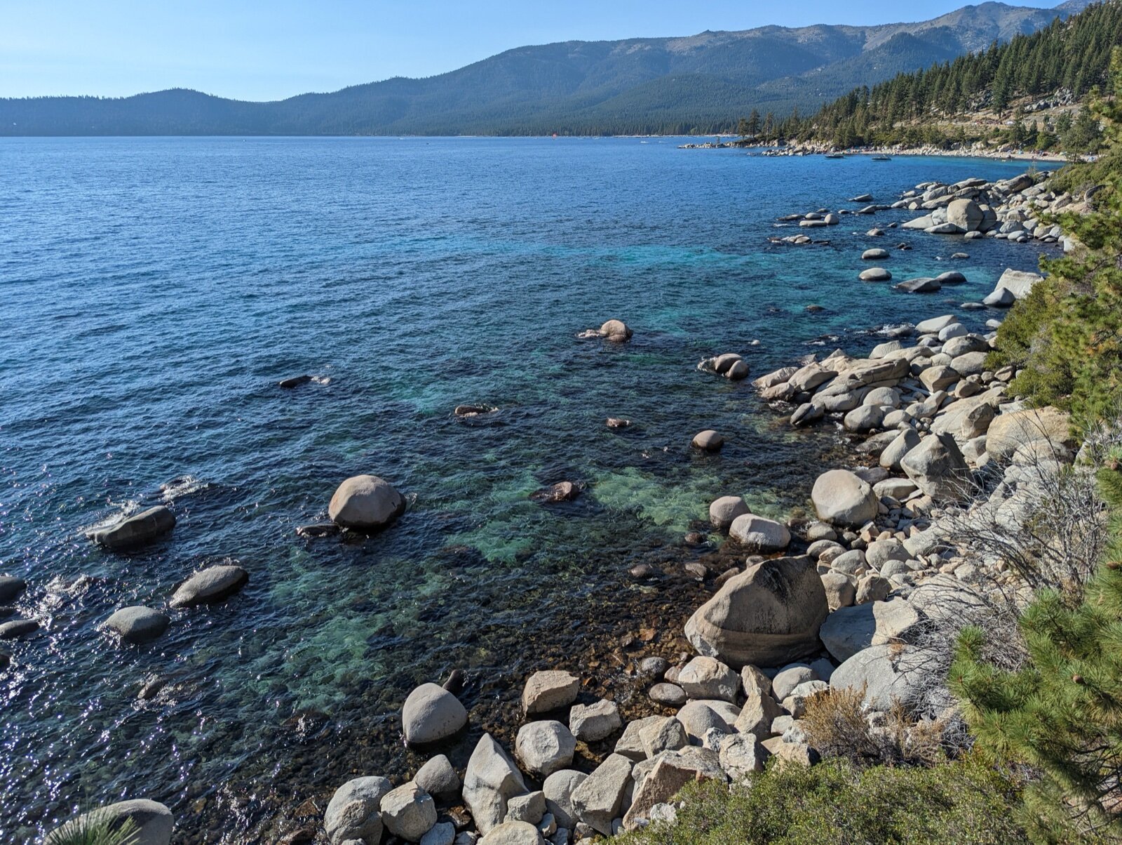 Clear turquoise water and granite boulders along the Nevada shore of Lake Tahoe, with pine-covered mountains across the lake