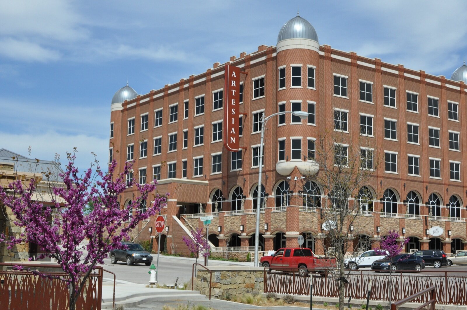 The red-brick Artesian Hotel in Sulphur, Oklahoma, with domed corner towers and a redbud tree in flower in the foreground