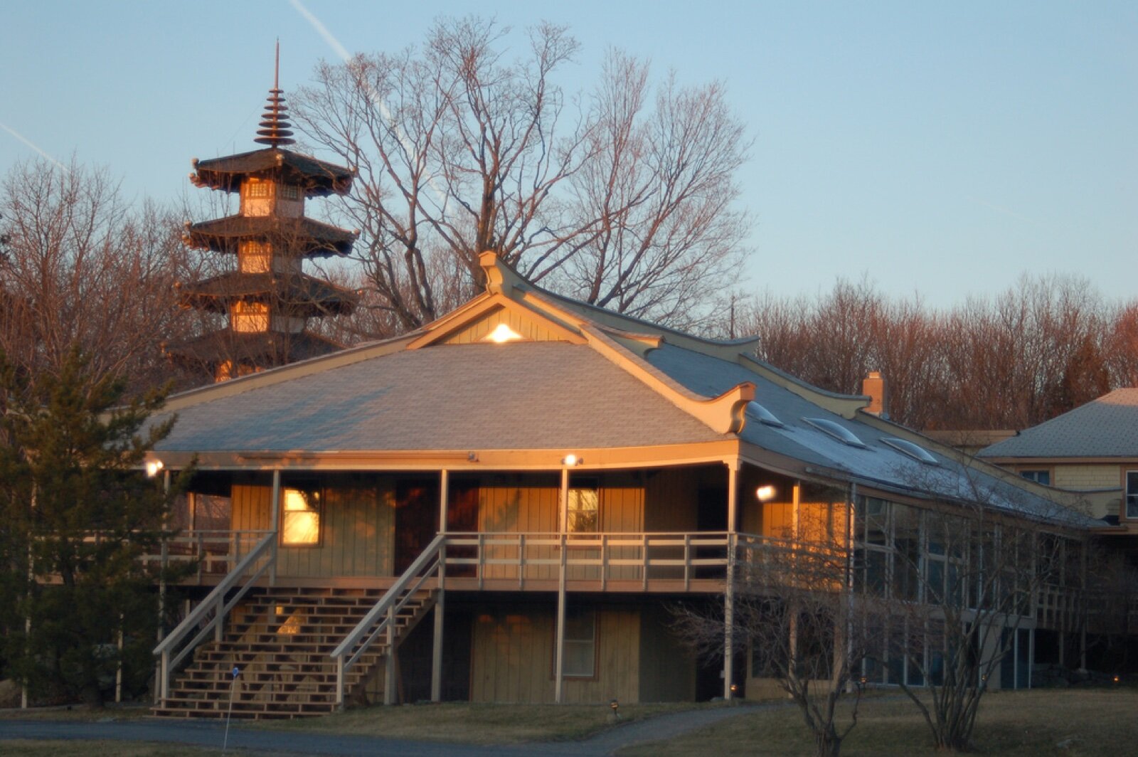The wooden main building of the Providence Zen Center with a tiered pagoda behind it, lit by low evening sun among bare trees