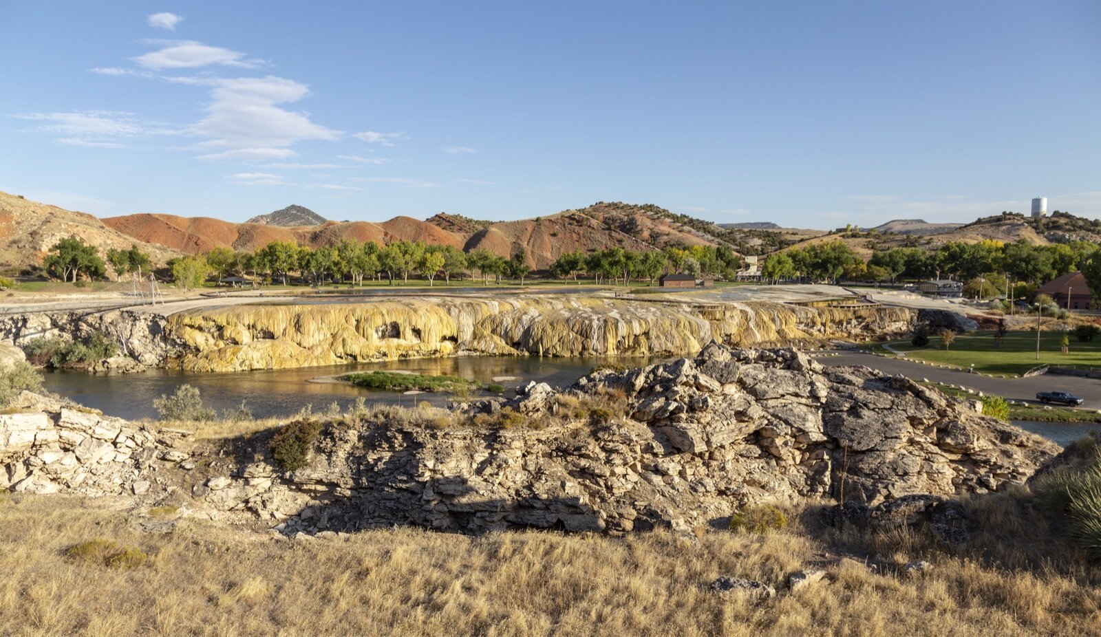 Mineral terraces in cream and orange running down to the Bighorn River at Hot Springs State Park, Thermopolis, with red hills behind