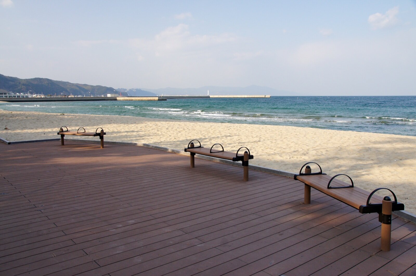 A wooden boardwalk with benches beside a sandy beach and calm sea on Awaji Island, Japan