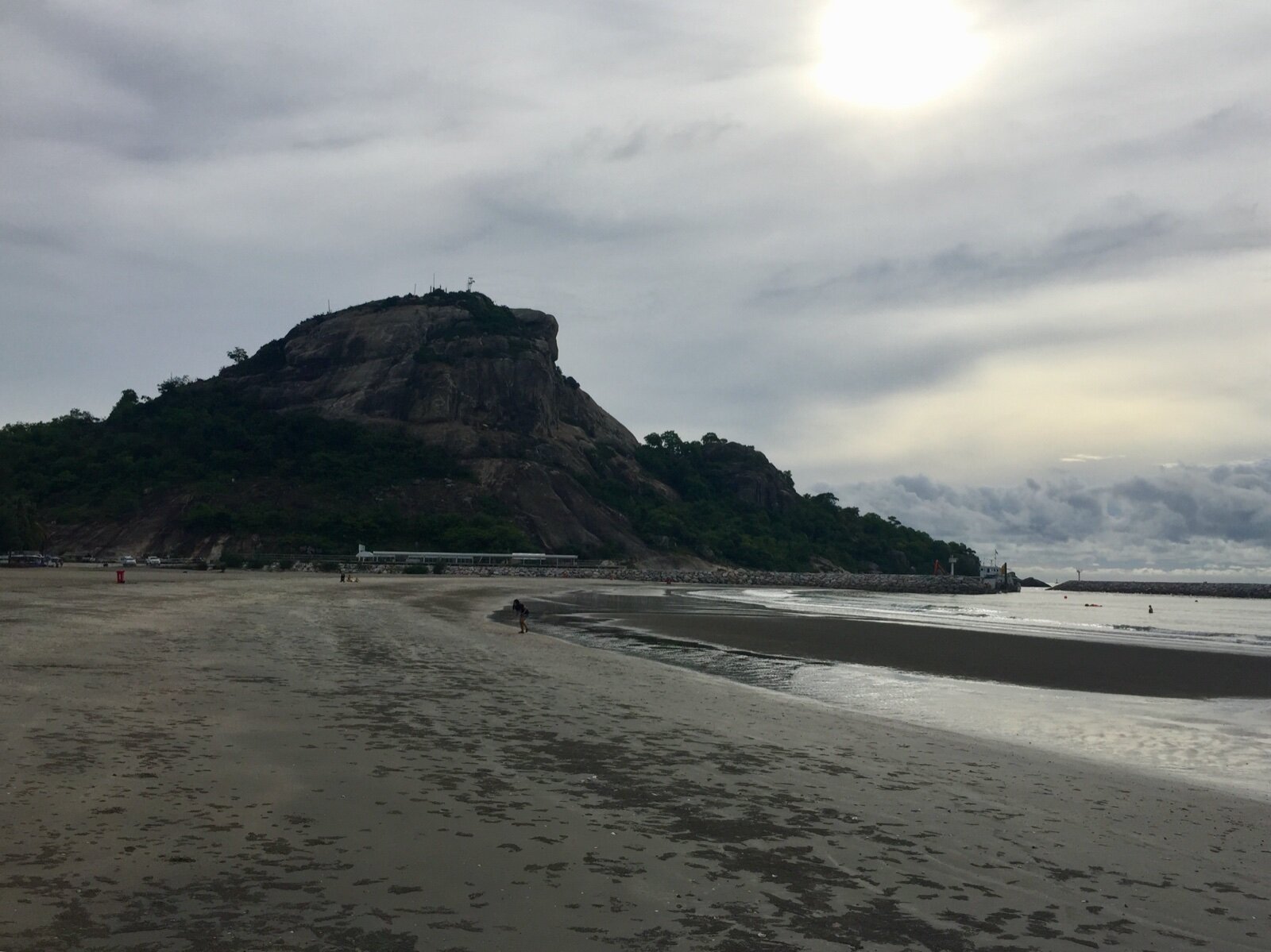 Khao Takiab hill rising above a wide sandy beach at low tide in Hua Hin, Thailand, under a cloudy sky